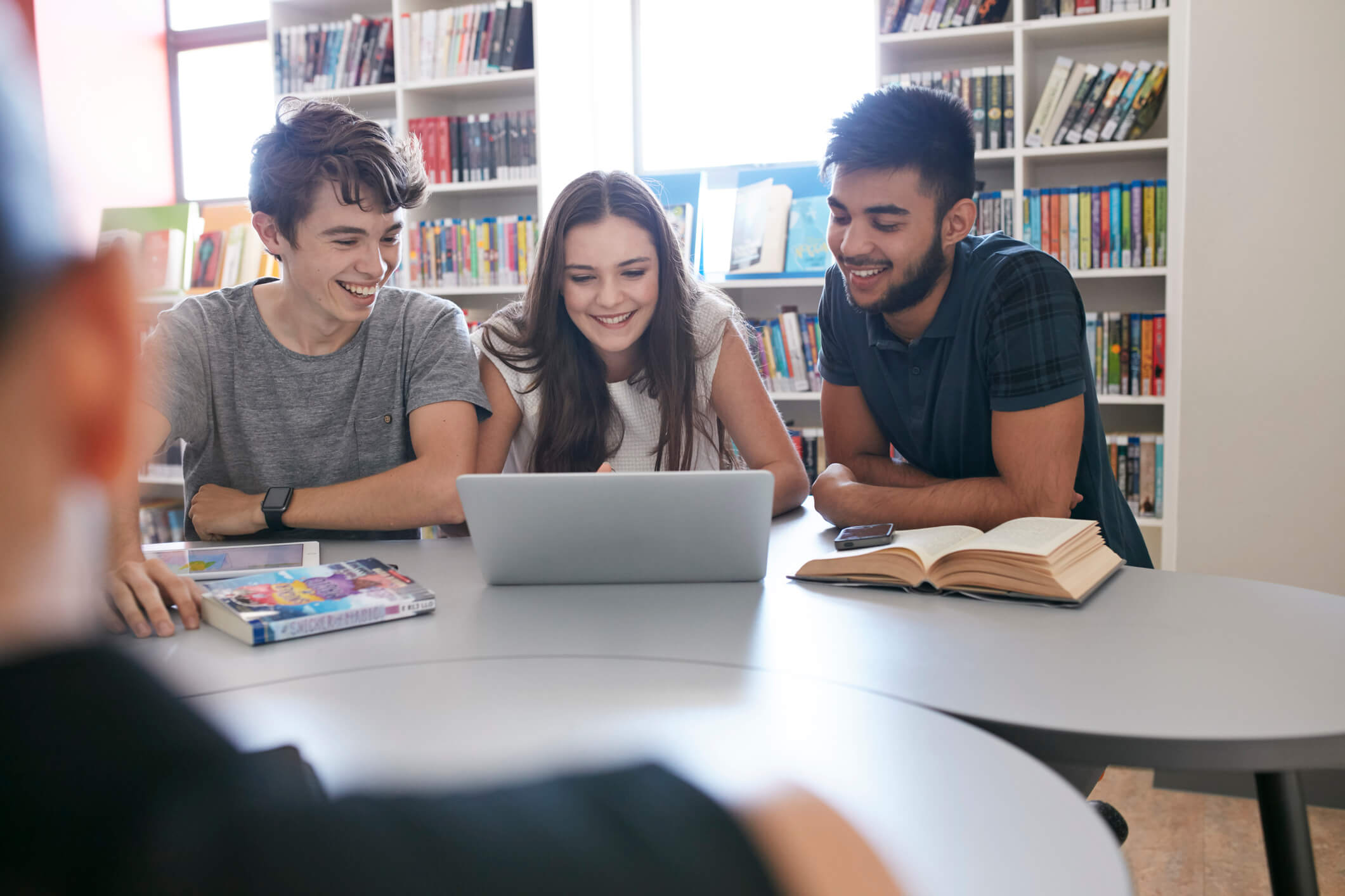 UX na educação: imagem representando três alunos na biblioteca da faculdade, estudando com um laptop