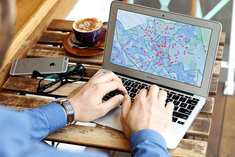 o que é geomarketing? conheça o software OnMaps. Homem utiliza laptop com uma imagem de um mapa na tela. Ao lado, um smartphone, um óculos e uma xícara de café